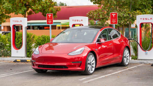 A red Tesla sedan charging in a parking lot.