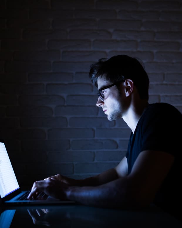 Man working on laptop in dark.