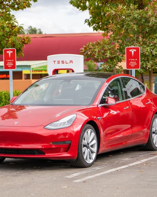 A red Tesla sedan charging in a parking lot.